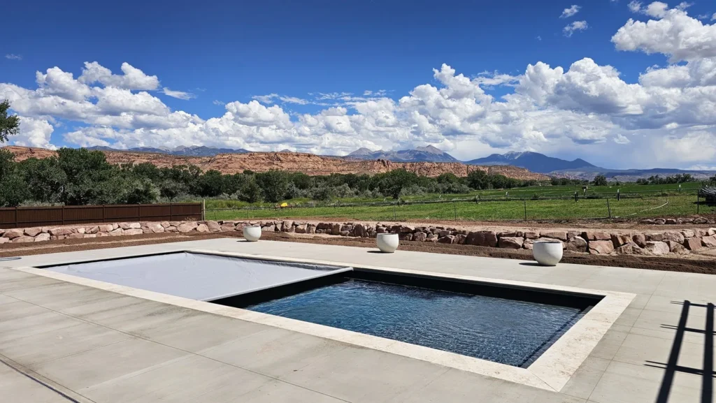 Long dark-finish pool with the automatic cover half open, white planters, and the La Sal Mountains