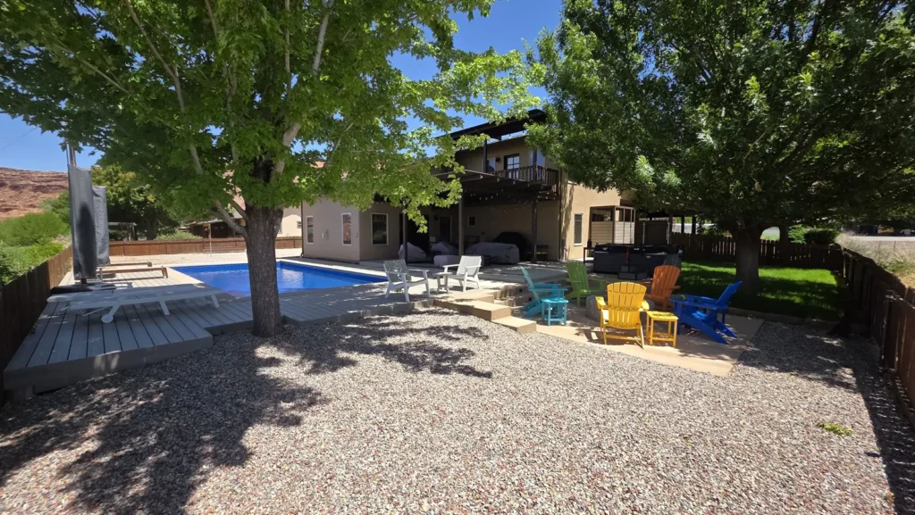 Shaded backyard with a bright blue pool, composite deck, and colorful Adirondack chairs around a fire pit