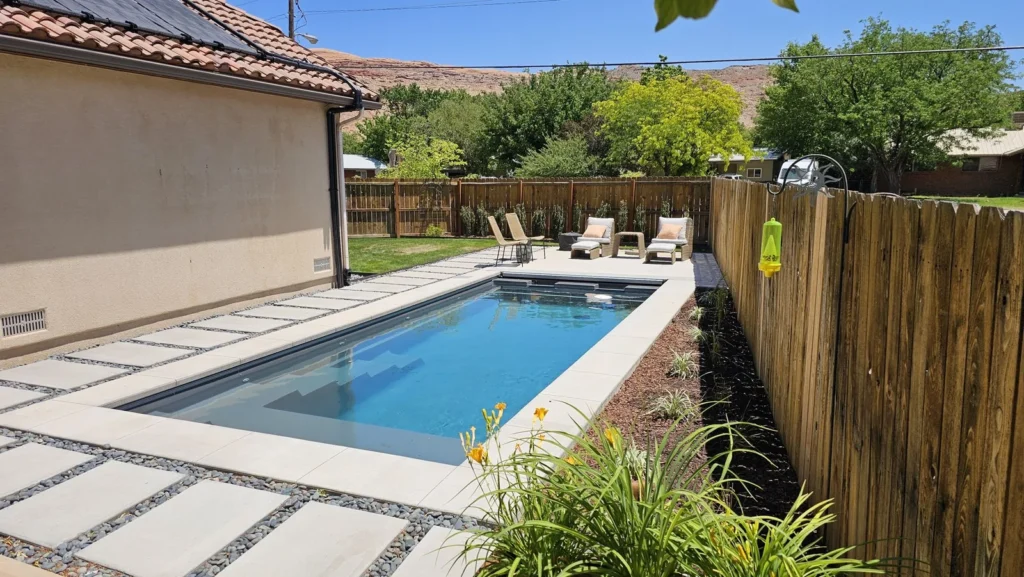 Narrow fiberglass pool seen from the far end, with full-width steps and solar collectors on the roof